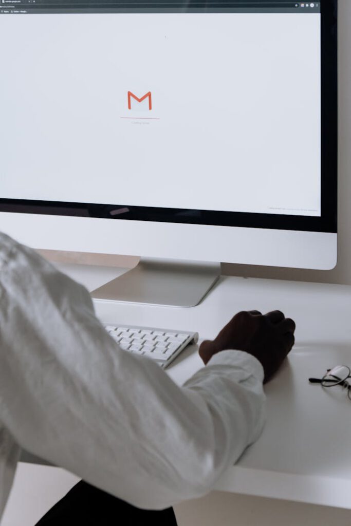 A professional in an office setting checking emails on a desktop computer with a clean workspace.