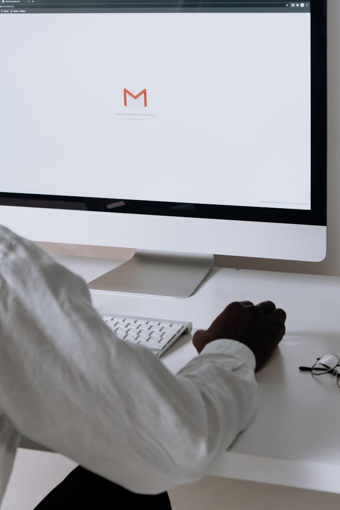 A professional in an office setting checking emails on a desktop computer with a clean workspace.